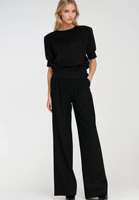 Czarna bluzka z krótkimi bufkami oraz czarne szerokie spodnie z zakładkami. Oba elementy wykonane są z gładkiego materiału, tworząc elegancką sylwetkę.