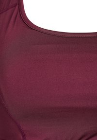 Sujetador deportivo granate con tejido liso y elástico; escote redondeado; y costuras planas a lo largo de las uniones, que crean un aspecto elegante.