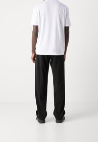 Camiseta blanca de algodón con mangas cortas, combinada con pantalones negros. La camiseta tiene una textura suave y los pantalones son holgados con un corte recto.