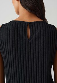 Top in tessuto nero a costine con chiusura a occhio di bue sul retro, dotata di un bottone nero rotondo. La superficie è morbida e leggermente pelosa.