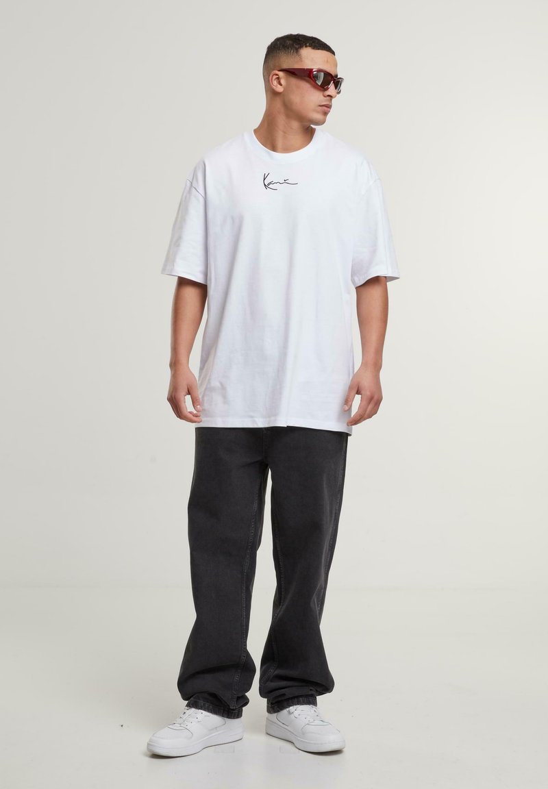 White cotton oversized t-shirt with brand logo, paired with dark gray wide-leg pants and white sneakers. Character wears dark sunglasses.