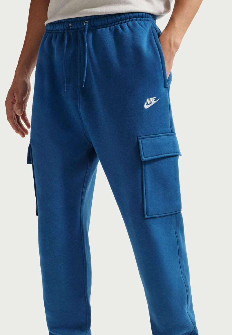 Pantalon de jogging bleu en tissu doux, avec une taille élastique à cordons, des poches latérales et un logo Nike blanc sur la cuisse.