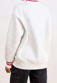 Felpa grigio chiaro con polsini e collo a coste a righe rosse e bianche, dal taglio ampio e tessuto morbido. Vista posteriore mostrata.