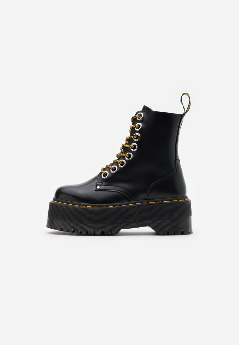 Botte de combat noire brillante avec une semelle plateforme épaisse, des coutures jaunes, des lacets jaunes et noirs, et une bride de tirage à l'arrière.
