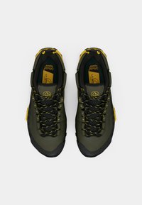 Πράσινα και μαύρα μποτάκια πεζοπορίας με κίτρινες κορδόνες και λεπτομέρειες, με υφασμάτινες επάνω επιφάνειες, μαξιλαρωτά πατάκια και ανθεκτική καουτσούκ σόλα.