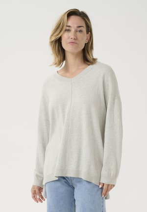Hellgrauer Strickpullover mit V-Ausschnitt, lässigen Schultern und seitlichen Schlitz. Hat eine weiche Textur und eine bequeme Passform. Kombiniert mit blauen Jeans.
