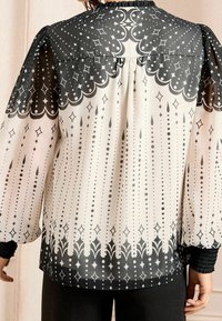 Genomskinlig blus i svart och kräm med en skaldjursmönster, vertikalt prickigt design och volangärmar. Löst passform med en elegant drapering.