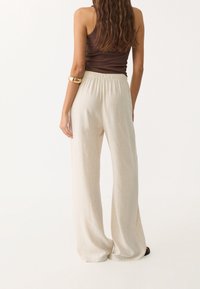 Pantalon beige à jambes larges avec une taille élastique, fabriqué dans un tissu léger, présentant une texture lisse et un design minimaliste.