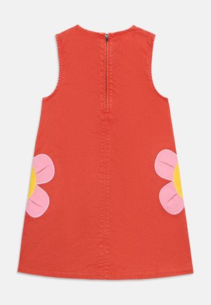 Αμάνικο κόκκινο φόρεμα με φερμουάρ στην πλάτη και μεγάλα ροζ και κίτρινα λουλουδένια διακοσμητικά σε κάθε πλευρά κοντά στο τελείωμα.