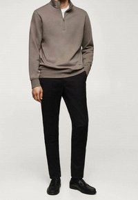 Gilet zippé marron clair avec une texture douce, associé à un pantalon slim noir et des chaussures en cuir noires. Design simple avec peu de détails.