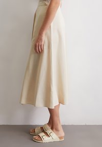 A beige, flared midi skirt made of lightweight fabric, paired with beige sandals featuring dual adjustable straps and a textured sole.