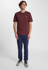 Bordeaux bomulds t-shirt med rund halsudskæring, parret med navy sweatpants og grå løbesko med blå detaljer.