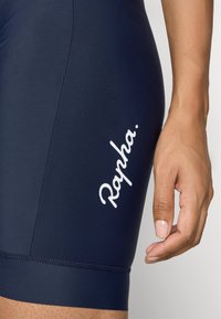 Marine cykelsorts lavet af strækstof, med et hvidt "Rapha." logo på siden, samt flade sømme ved benåbningerne.