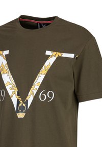 Olijfgroene katoenen t-shirt met een grote witte en gouden "V" grafiek met sierlijke details en het nummer "69" eronder. Ronde halslijn.