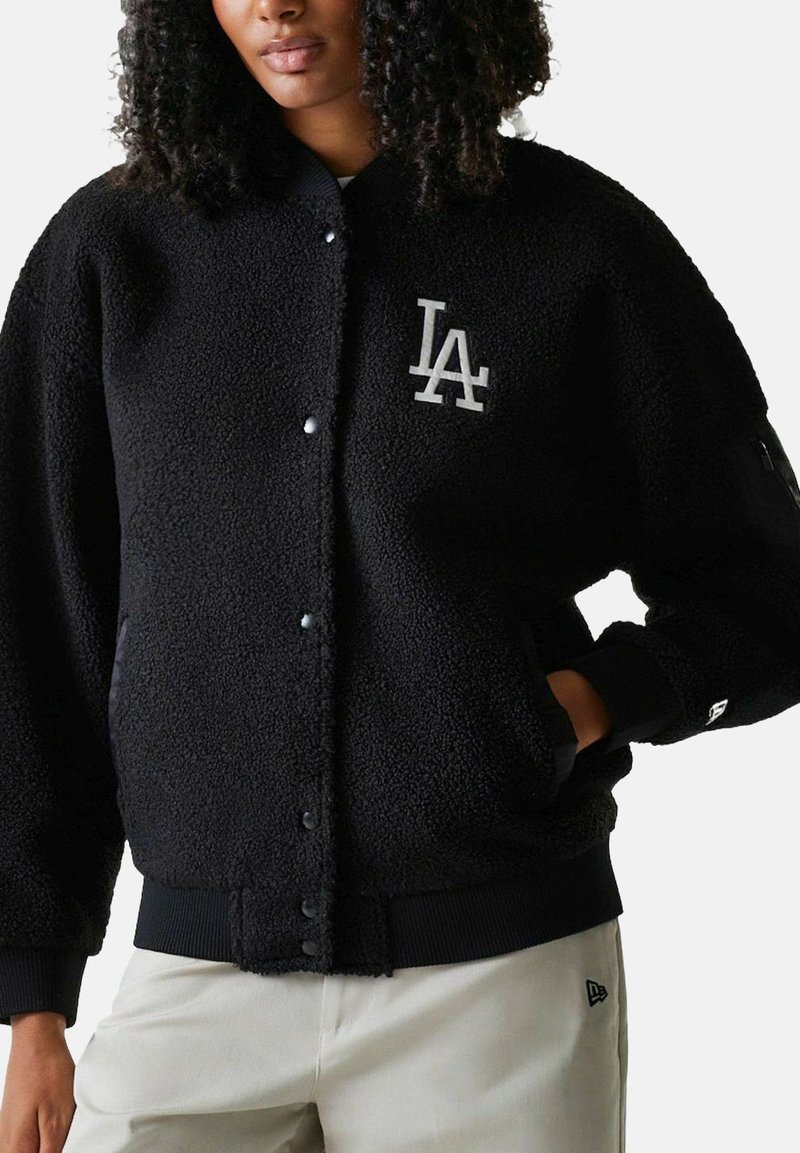 Schwarze Fleecejacke mit durchgehendem Knopfverschluss, gerippten Bündchen und einem Logo auf der Brust. Weiche Textur und lockerer Sitz, mit Seitentaschen.