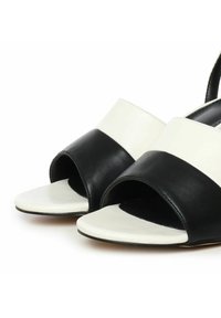 Sandalias de cuero en blanco y negro con un diseño de punta abierta, que cuentan con anchas correas de colores y una textura suave.