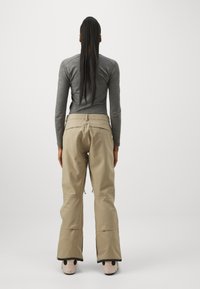 Pantalons de neige beiges avec une coupe décontractée, fabriqués en matériau imperméable, dotés de fermetures éclair au niveau des chevilles et d'une taille plate.