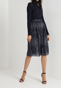 Haut à manches longues côtelé bleu marine associé à une jupe sombre paillettée de longueur genou avec un design plissé et une taille élastique. Talons noirs à lanières.