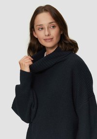 Ciemnoniebieski, oversize sweter o ribbowanej fakturze, z dużym dekoltem w kształcie czwórki i szerokimi rękawami. Miękka tkanina z delikatnymi detalami.