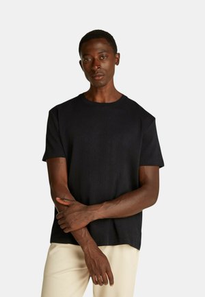 T-shirt nera realizzata in tessuto testurizzato, con scollo rotondo e maniche corte, abbinata a pantaloni di colore chiaro.