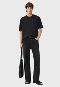 Sort oversized t-shirt med en lomme, kombineret med mørke jeans med lige ben og sorte sko. En sort skuldertaske bæres.