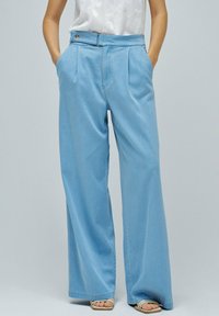 Pantalons larges bleu clair avec des plis, dotés d'une fermeture à bouton à l'avant et de poches latérales, fabriqués en denim doux.
