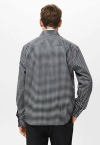 Camisa de manga larga a cuadros en negro y gris, con un cuello clásico, puños abotonados y un detalle de yugo en la parte posterior.
