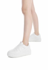 Zapatillas blancas con una textura de cuero suave, punta perforada, suela gruesa y cordones redondos. Diseño minimalista con un discreto detalle del logo.