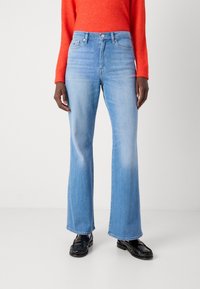 Høytlivede lyseblå slengjeans laget av denim, med frontknapp-lukking og subtil falming på stoffet. Akkompagnert av blanke svarte sko.
