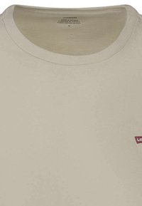 Camiseta de algodón beige con cuello redondo y mangas cortas, que presenta un pequeño logo rojo de Levi's en la parte izquierda del pecho. Textura suave.