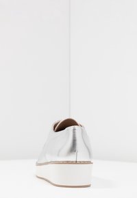 Chaussure décontractée métallique argentée avec un bout arrondi, une semelle plateforme blanche et sans lacets visibles. Texture lisse avec un design élégant.