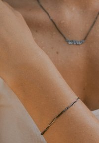 Silberne Kettenarmband mit einem zarten, länglichen Glieddesign, das auf einem gebräunten Handgelenk ruht. Schlicht und minimalistisch ohne Verzierungen.