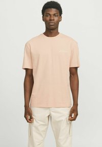 Lichtroze katoenen T-shirt met een ronde hals en korte mouwen; heeft een klein wit logo op de borst; gladde textuur.