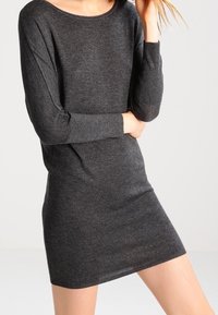 Abito grigio a maglia con maniche lunghe e vestibilità rilassata. Presenta un ampio scollo e una consistenza morbida, che termina sopra la metà della coscia.