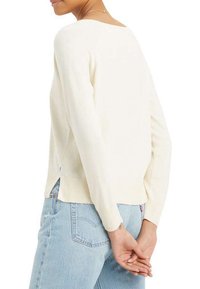 Pull en tricot de couleur crème avec des manches longues, un large encolure et des détails côtelés au niveau de l'ourlet. Porté avec un jean bleu clair.