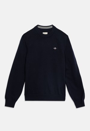 Pull bleu marine à manches longues avec col rond, poignets et ourlet côtelés, petit logo brodé sur la poitrine gauche et encolure intérieure à rayures.