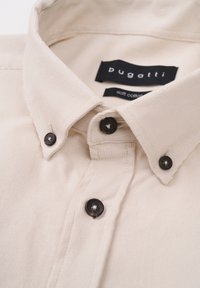 Beige shirt with a soft cotton texture, black buttons, and a folded collar; includes a label reading "bugatti soft cotton."
