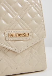 Borsa a tracolla in ecopelle beige trapuntata con flap triangolare, plaque in tonalità oro "Love Moschino" e motivo a diamante cucito.