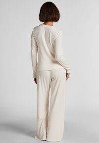 Cream ribbed knit loungewear set, consisting of a long-sleeve top with a rounded neckline and wide-leg pants, featuring a soft, textured fabric.
