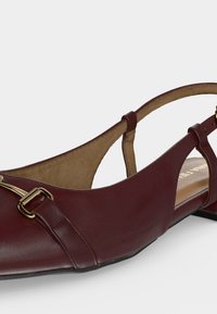 Επίπεδο παπούτσι από δέρμα βουργουνδίας με μυτερή μύτη, λουράκι στο πίσω μέρος, χαμηλό τακούνι και χρυσή λεπτομέρεια με σχέδιο αλόγου στο επάνω μέρος.