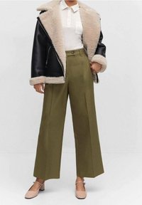 Veste en simili cuir noir avec doublure en fausse fourrure crème, polo blanc, pantalon large vert olive et ballerines rose clair.