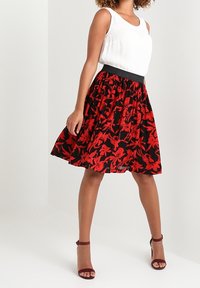 Jupe à imprimé floral avec un fond noir, ornée de fleurs rouges, taille élastique et silhouette évasée. Associée à un haut blanc.
