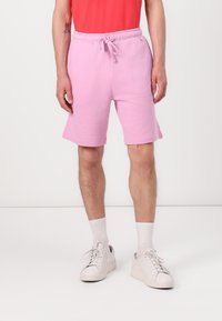 Ljust rosa bomullsblandade shorts med elastisk midja och justerbar snörning; bärs med vita strumpor och ljusa sneakers.