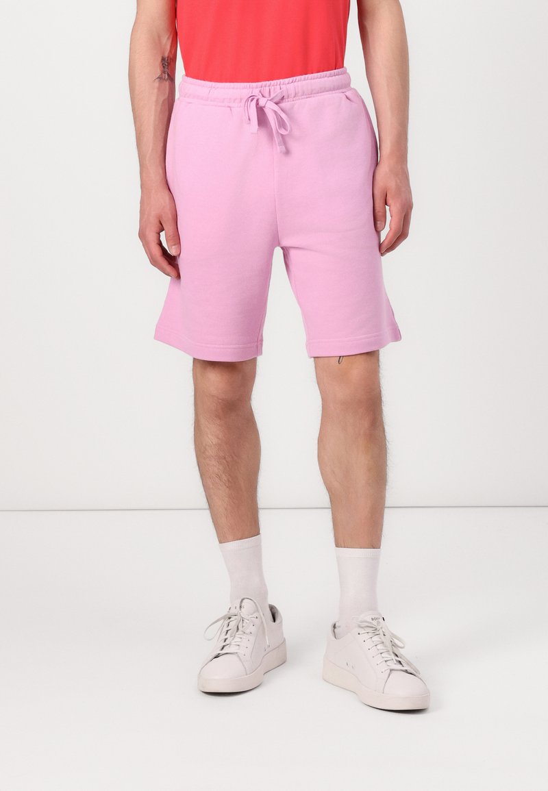 Ljust rosa bomullsblandade shorts med elastisk midja och justerbar snörning; bärs med vita strumpor och ljusa sneakers.