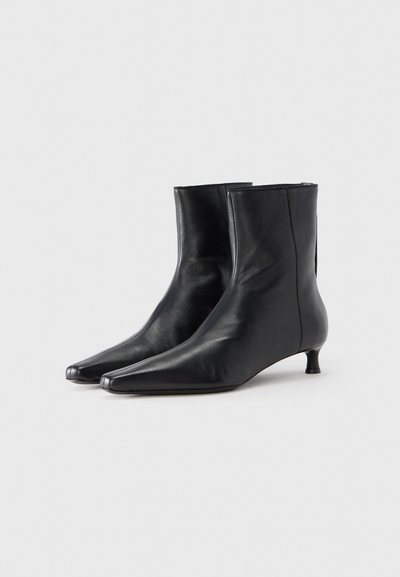Μαύρα δερμάτινα μποτάκια αστραγάλου με μυτερή μύτη, χαμηλό τακούνι, λεία υφή και μινιμαλιστική εμφάνιση. Διαθέτουν ραφή στο πλάι χωρίς ραφές.