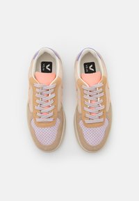 Paire de baskets beige, lavande et pêche avec une zone des orteils perforée, des lacets blancs et des semelles intérieures noires portant la mention « Veja », vues de dessus.