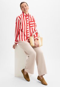 Striped red and white button-up shirt, beige wide-leg pants, brown suede loafers, and a small woven handbag with light handles.