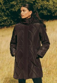 Tmavohnedý prešívaný kabát s vysokým golierom, dlhými rukávmi a bočnými vreckami, s elegantnou, hladkou textúrou a štruktúrovaným dizajnom.