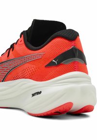 Roter Sportschuh mit einem Obermaterial aus Mesh und schwarzen Akzenten, strukturiertem Sohlenprofil und reflektierenden silbernen Streifen. Auffällige Markenzeichen am Fersenbereich und an der Sohle.
