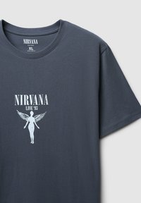 T-shirt di cotone grigio scuro con stampa grafica bianca di una figura con ali e la scritta "NIRVANA LIVE '93" sopra, colletto a giro.